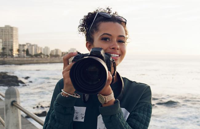 woman holding a camera with lake or ocean behind her